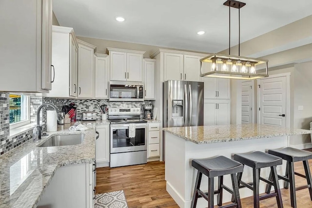 kitchen featuring hanging light fixtures, sink, light hardwood / wood-style flooring, stainless steel appliances, and a center island