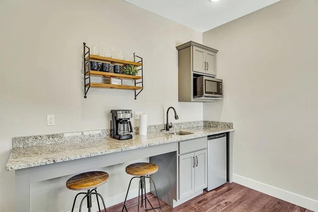 kitchen with sink, dark wood-type flooring, gray cabinets, stainless steel appliances, and light stone countertops