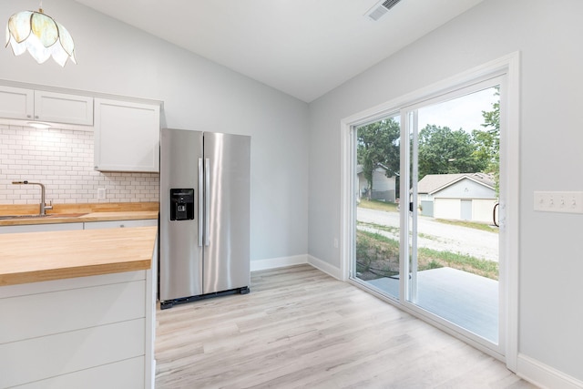 kitchen with butcher block counters, white cabinetry, vaulted ceiling, and stainless steel refrigerator with ice dispenser