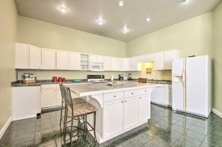 kitchen with dark tile patterned floors, white appliances, an island with sink, white cabinets, and a kitchen bar