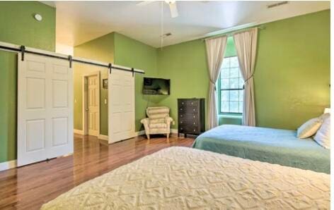 bedroom featuring ceiling fan, hardwood / wood-style floors, and a barn door