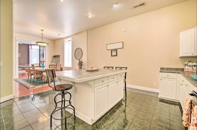 kitchen featuring a center island, white cabinets, pendant lighting, a breakfast bar area, and tile countertops