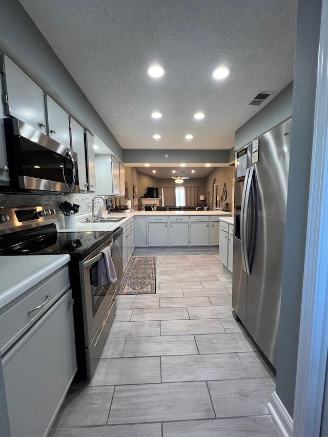 kitchen featuring gray cabinetry, kitchen peninsula, backsplash, appliances with stainless steel finishes, and a textured ceiling