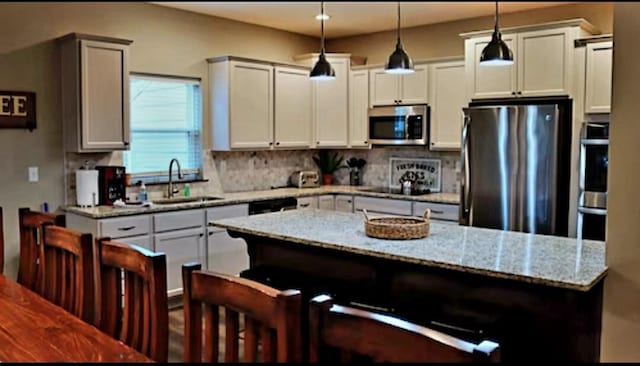 kitchen with hanging light fixtures, sink, stainless steel appliances, a kitchen breakfast bar, and light stone countertops