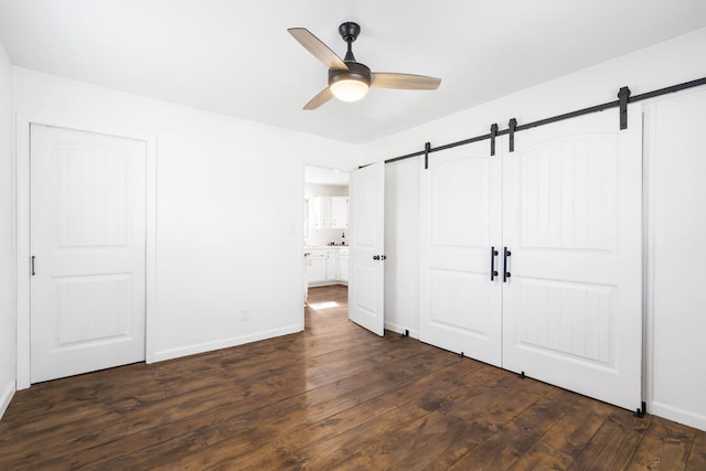 unfurnished bedroom featuring connected bathroom, a closet, a barn door, dark hardwood / wood-style flooring, and ceiling fan