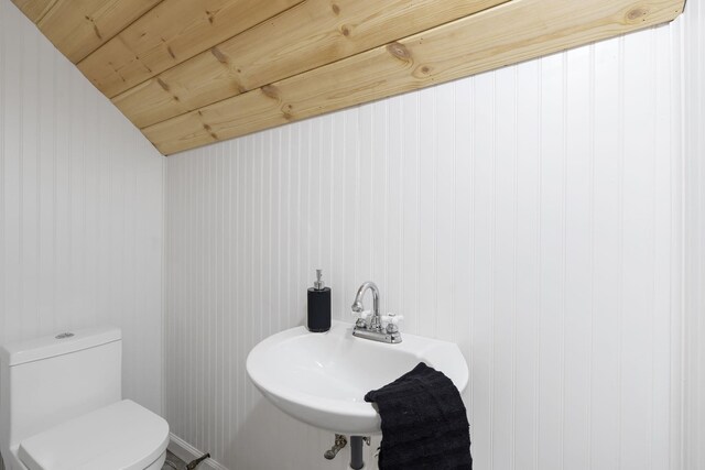 bathroom featuring toilet, wood walls, sink, and wooden ceiling