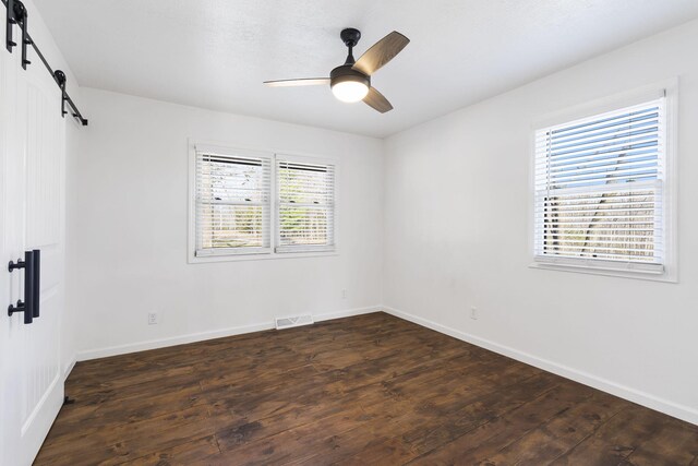 empty room featuring a barn door, dark wood-type flooring, and plenty of natural light