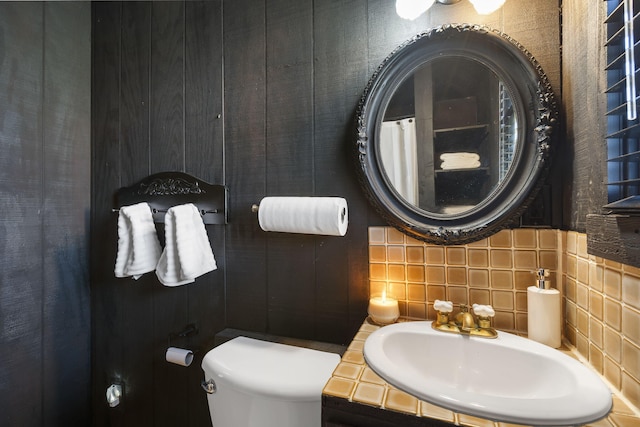 bathroom featuring backsplash, tile walls, sink, and toilet