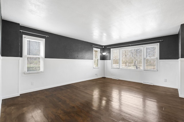 unfurnished room with a textured ceiling, dark wood-type flooring, and plenty of natural light