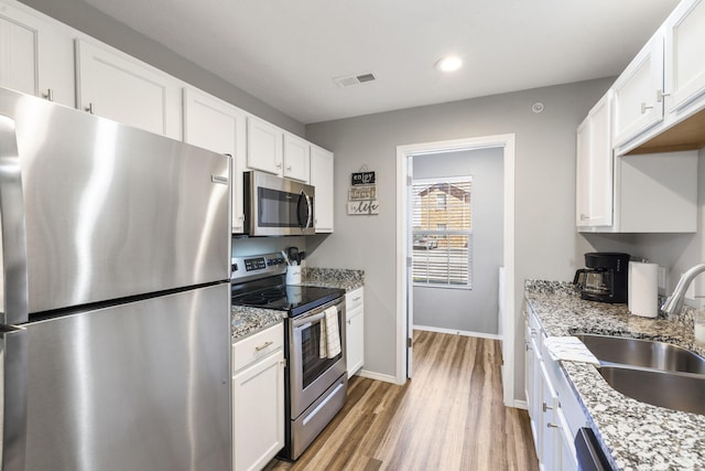 kitchen featuring light stone counters, sink, light hardwood / wood-style floors, white cabinetry, and appliances with stainless steel finishes