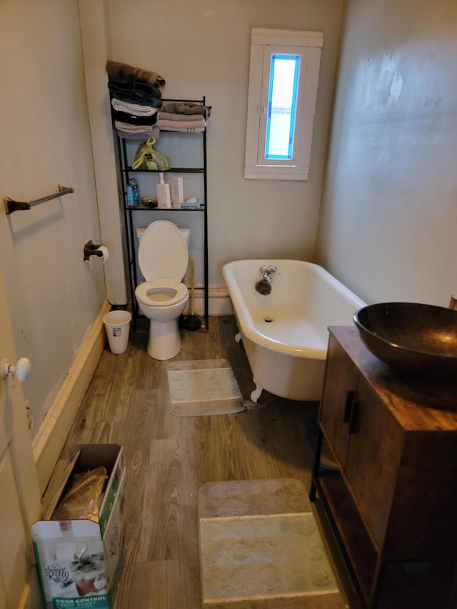 bathroom with wood-type flooring, a tub to relax in, vanity, and toilet