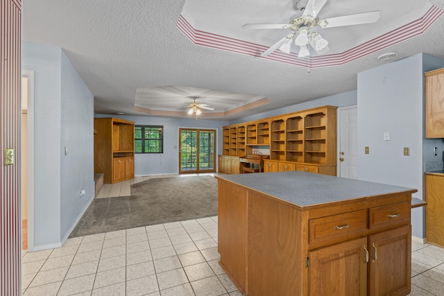 kitchen with ceiling fan, light colored carpet, a kitchen island, a raised ceiling, and a textured ceiling