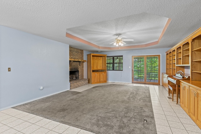 unfurnished living room with ceiling fan, a raised ceiling, a brick fireplace, a textured ceiling, and light colored carpet