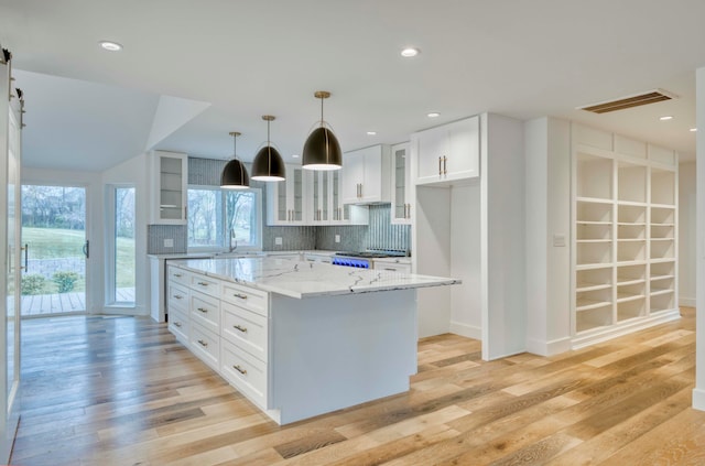 kitchen with light hardwood / wood-style floors, tasteful backsplash, light stone countertops, a center island, and white cabinetry