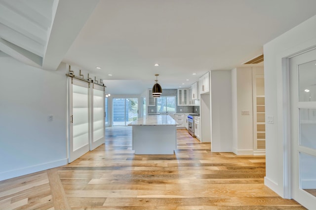 kitchen featuring a barn door, light hardwood / wood-style floors, stainless steel range oven, hanging light fixtures, and white cabinets