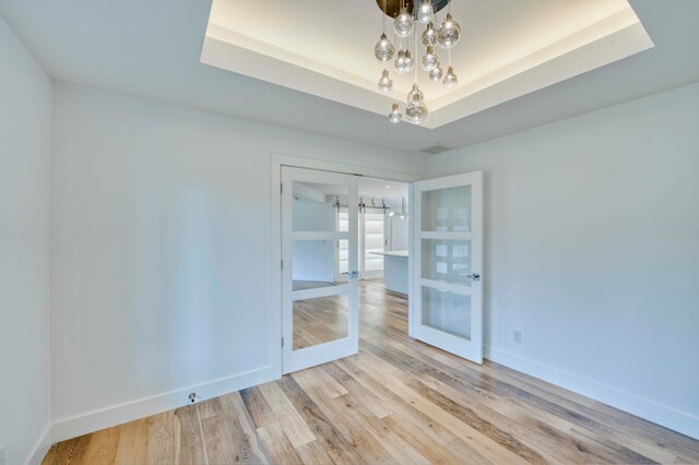 empty room with a notable chandelier, light wood-type flooring, and a tray ceiling