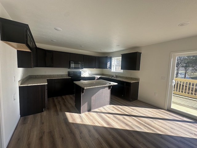 kitchen with a kitchen island, black microwave, dark cabinets, and wood finished floors