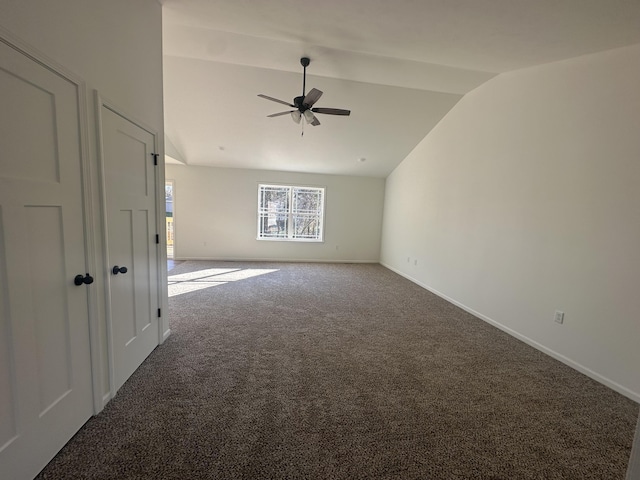 carpeted spare room featuring a ceiling fan, vaulted ceiling, and baseboards