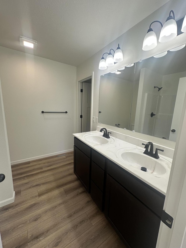 full bathroom with a textured ceiling, wood finished floors, walk in shower, and a sink