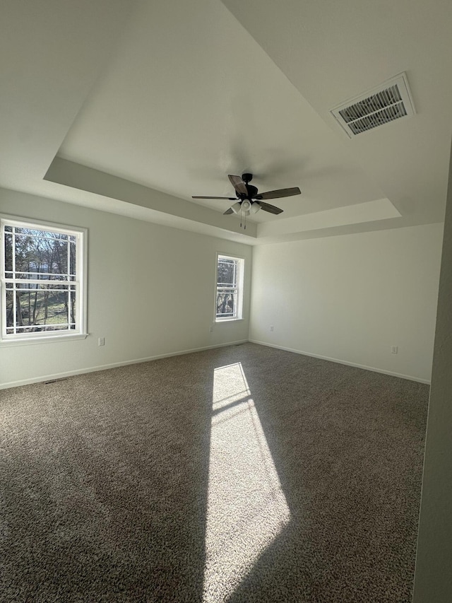 carpeted spare room featuring ceiling fan, baseboards, visible vents, and a raised ceiling