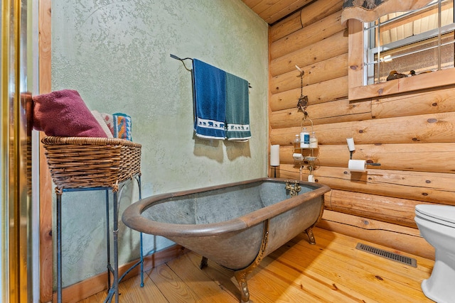 bathroom featuring a bathtub, rustic walls, toilet, and wood-type flooring