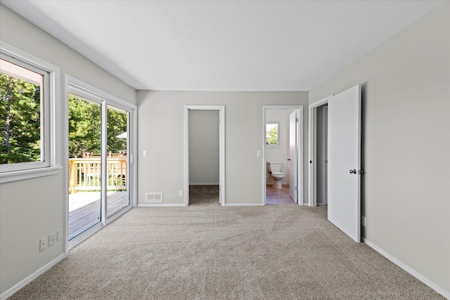 unfurnished bedroom featuring access to exterior, a spacious closet, connected bathroom, and light colored carpet