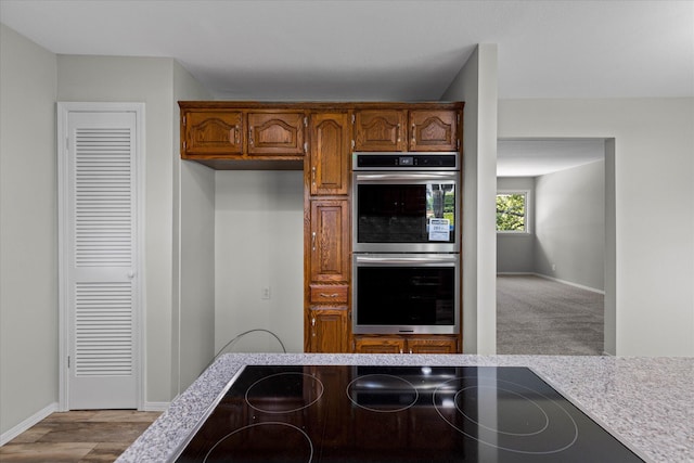 kitchen with black electric cooktop, stainless steel double oven, and light hardwood / wood-style floors