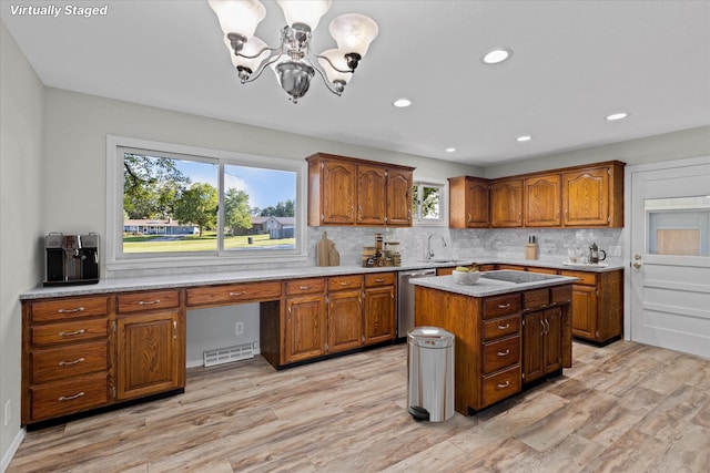 kitchen with tasteful backsplash, a kitchen island, stainless steel dishwasher, a notable chandelier, and light wood-type flooring