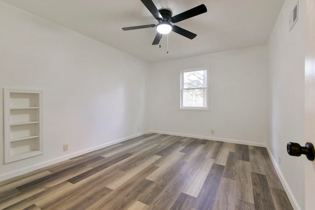 empty room featuring ceiling fan, built in features, and dark wood-type flooring