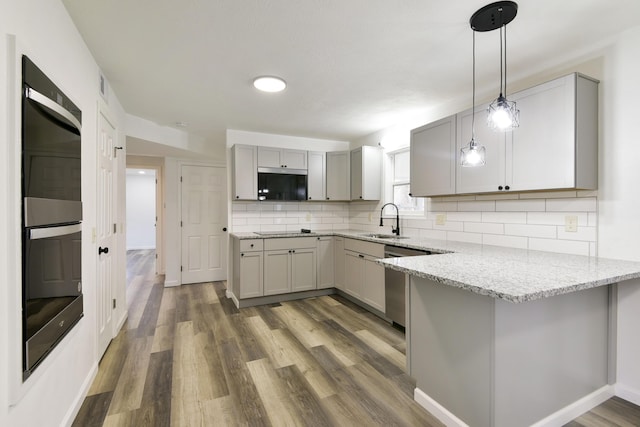 kitchen with a sink, black appliances, decorative backsplash, a peninsula, and gray cabinetry