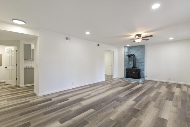 unfurnished living room with wood finished floors, visible vents, recessed lighting, and a wood stove