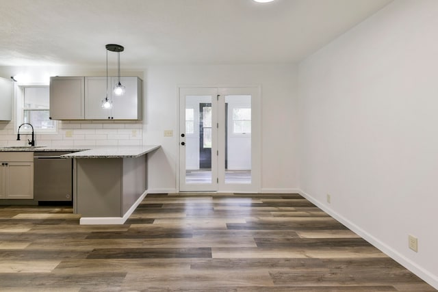 kitchen featuring light stone counters, pendant lighting, stainless steel dishwasher, dark hardwood / wood-style flooring, and decorative backsplash