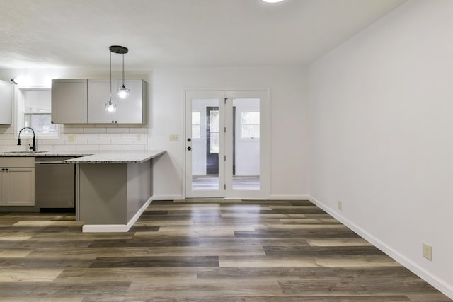 kitchen featuring backsplash, stainless steel dishwasher, a sink, light stone countertops, and gray cabinetry