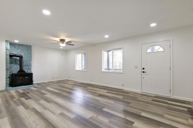 unfurnished living room featuring wood finished floors, a wood stove, baseboards, and ceiling fan