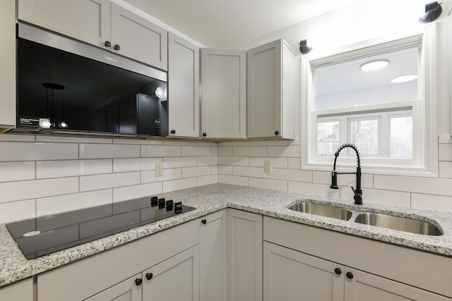 kitchen featuring black electric cooktop, a sink, stainless steel microwave, and tasteful backsplash