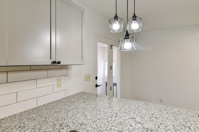interior space featuring pendant lighting, light stone counters, and tasteful backsplash