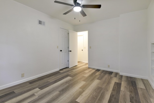 unfurnished room with baseboards, wood finished floors, visible vents, and a ceiling fan