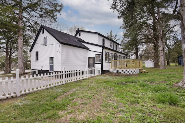 back of house with a lawn, a deck, an outdoor structure, fence, and a storage unit
