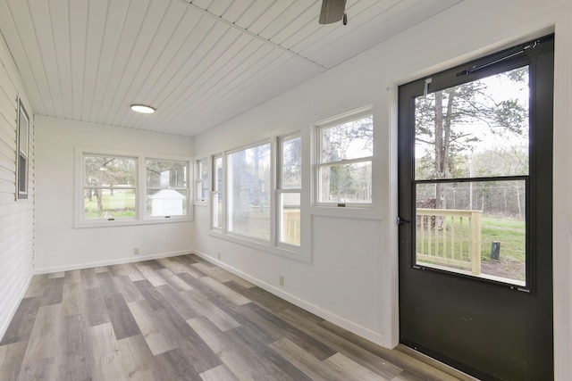 unfurnished sunroom featuring baseboards, wood finished floors, and plenty of natural light