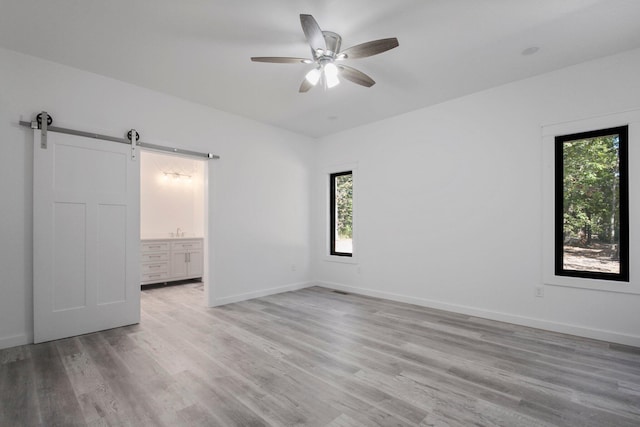 unfurnished bedroom featuring a barn door, light wood-type flooring, multiple windows, and ceiling fan