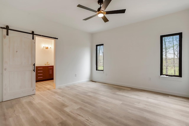 unfurnished bedroom featuring ensuite bathroom, multiple windows, ceiling fan, and a barn door