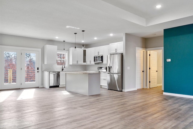 kitchen with a kitchen island, stainless steel appliances, white cabinets, light hardwood / wood-style floors, and decorative light fixtures