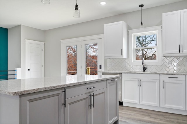 kitchen with light stone countertops, decorative light fixtures, light hardwood / wood-style flooring, and white cabinetry