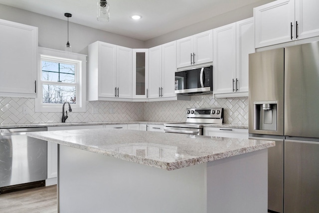 kitchen featuring light wood-type flooring, light stone countertops, stainless steel appliances, white cabinets, and hanging light fixtures