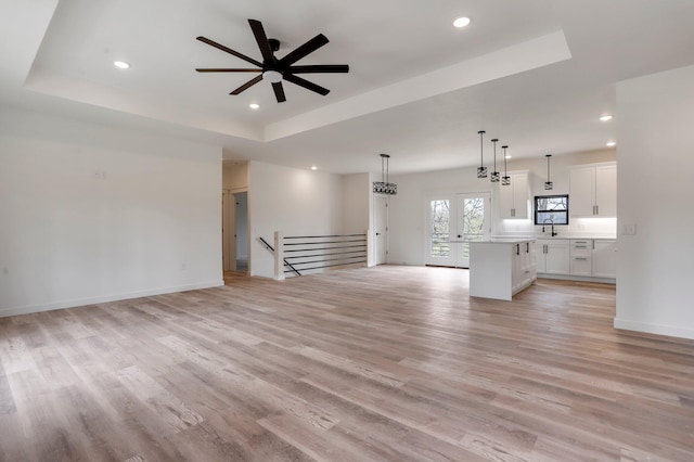 unfurnished living room with a tray ceiling, light hardwood / wood-style flooring, and ceiling fan