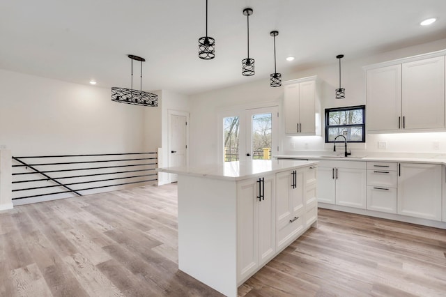 kitchen with sink, a kitchen island, decorative light fixtures, white cabinetry, and light hardwood / wood-style floors