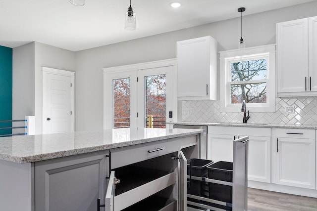 kitchen with light wood-type flooring, light stone countertops, decorative light fixtures, and white cabinets