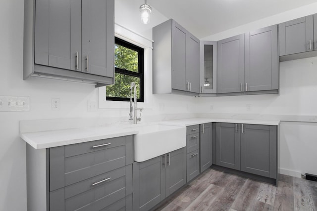 kitchen featuring gray cabinetry, light stone counters, hardwood / wood-style flooring, and sink