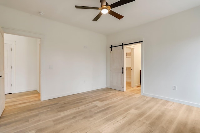 empty room with ceiling fan, light hardwood / wood-style floors, and a barn door