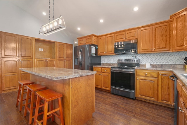 kitchen with appliances with stainless steel finishes, a kitchen island, a kitchen bar, and dark wood-type flooring